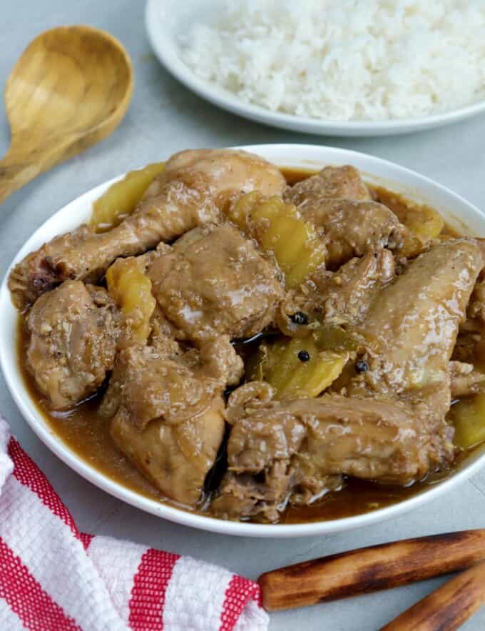 Chicken Adobo with potatoes in a serving bowl with a plate of steamed rice on the side