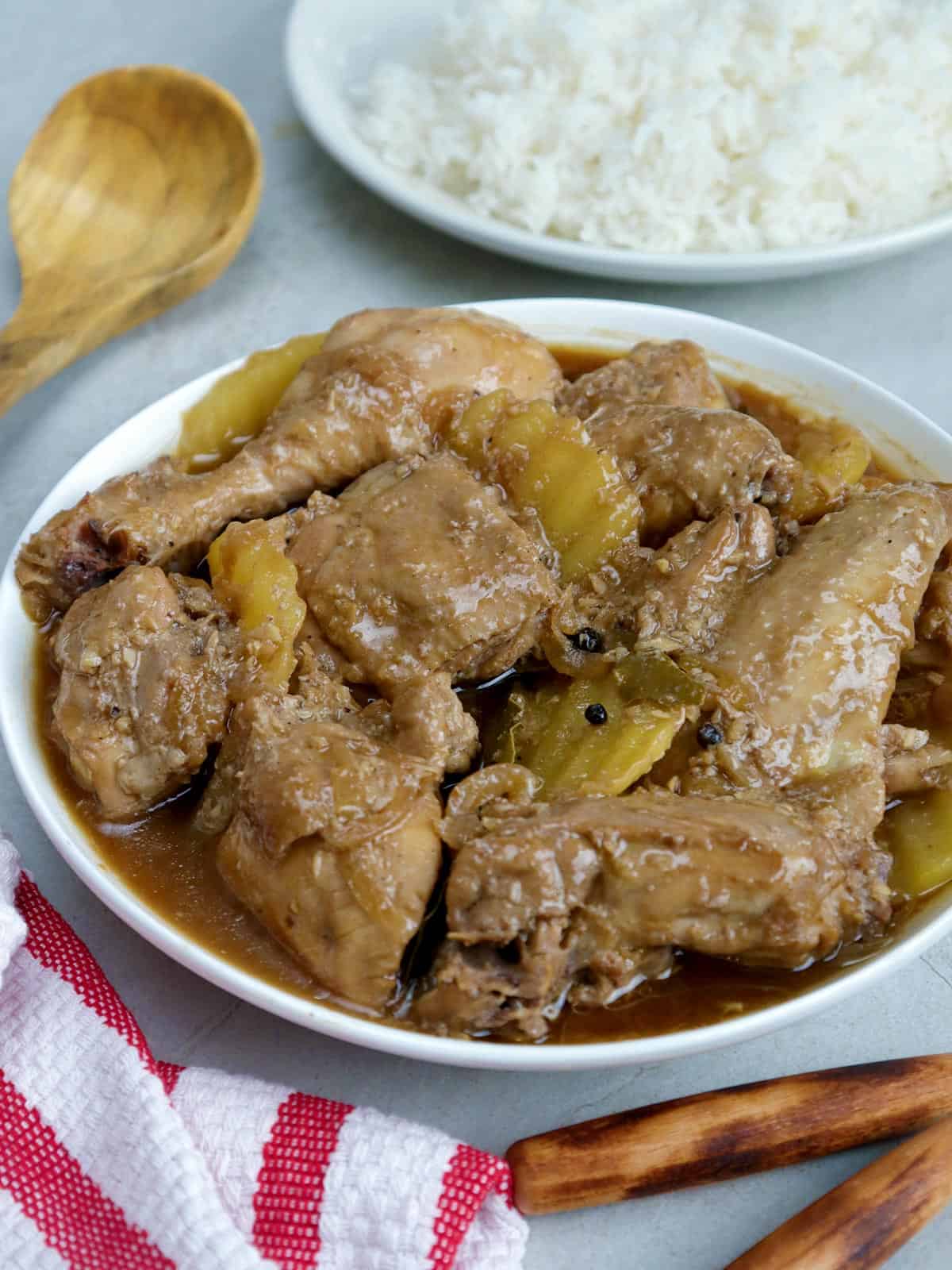 Chicken Adobo with potatoes in a serving bowl with a plate of steamed rice on the side