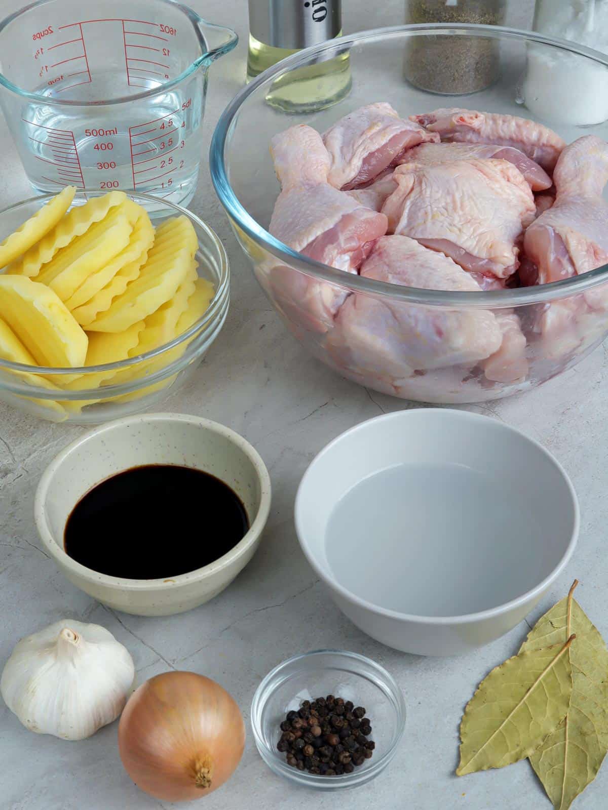 cut-up chicken, sliced potatoes, vinegar, soy sauce, water, onion, bay leaves, garlic, peppercorns in bowls