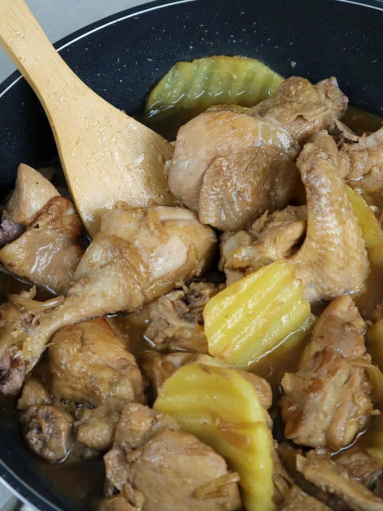 adobong manok in a pan with fried potatoes