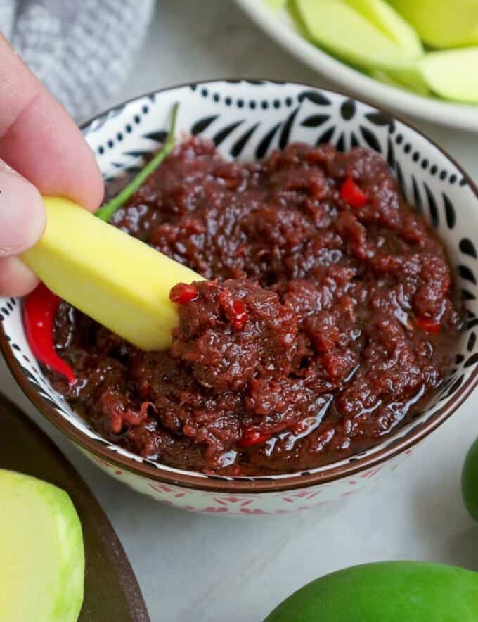 dipping sliced green mangoes in a bowl of ginisang bagoong