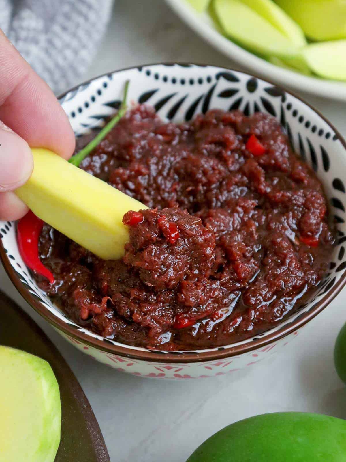 dipping sliced green mangoes in a bowl of ginisang bagoong