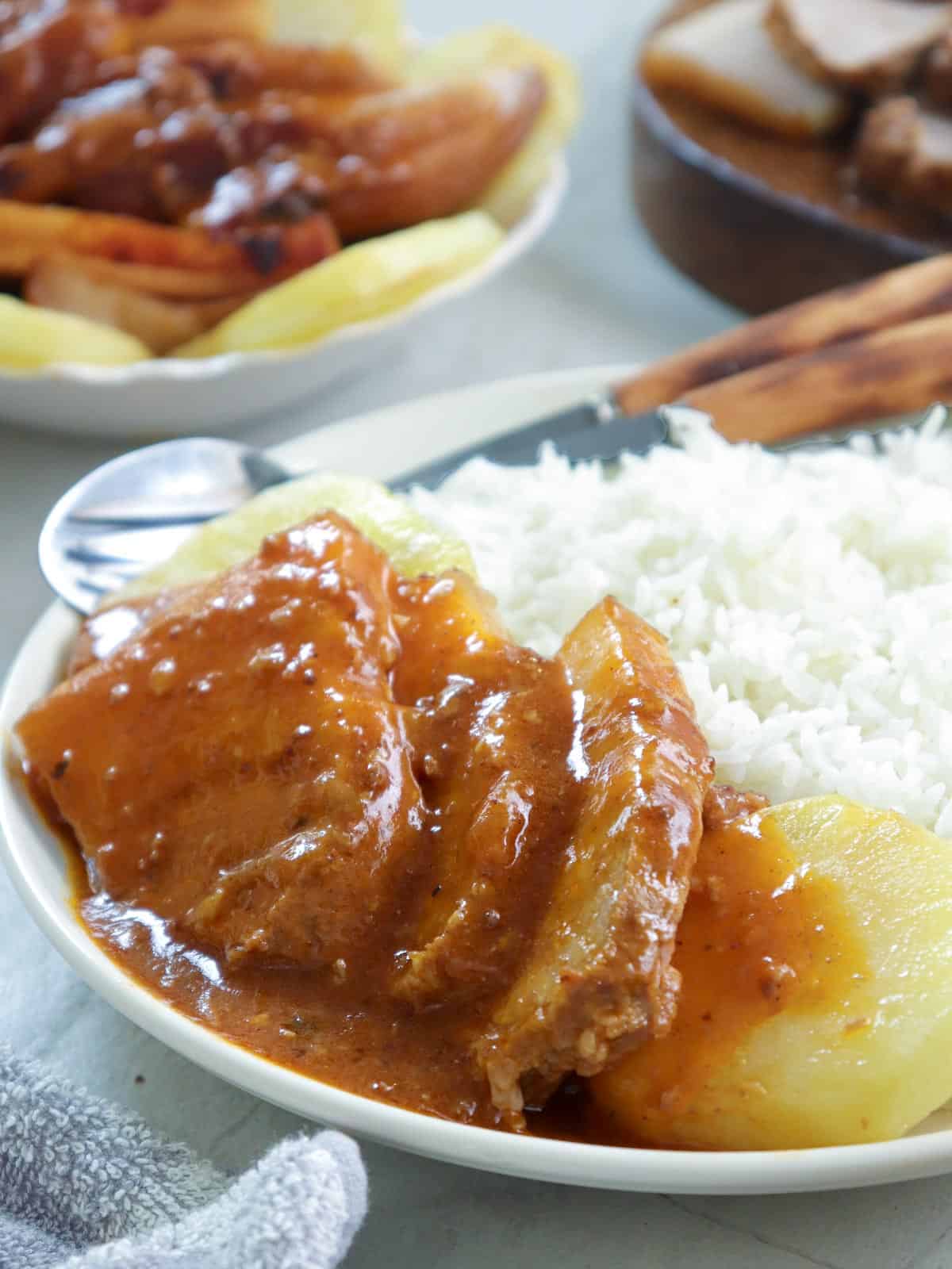 sliced pork asado, pan-fried potatoes and thick tomato gravy with steamed rice on a white plate