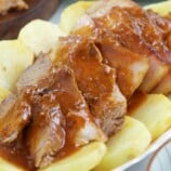 sliced Kapampangan-style asado with fried potato slices and tomato gravy on a serving platter