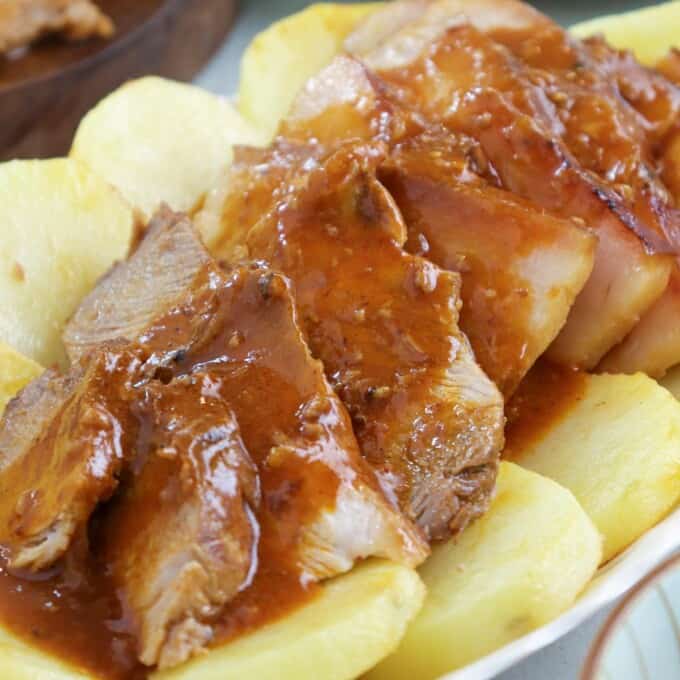 sliced Kapampangan-style asado with fried potato slices and tomato gravy on a serving platter