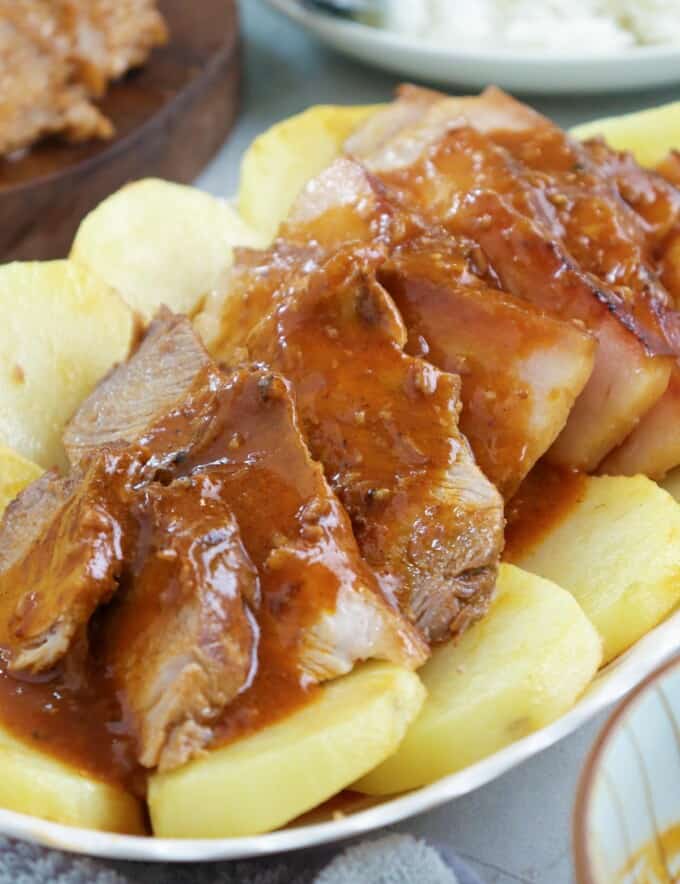 sliced Kapampangan-style asado with fried potato slices and tomato gravy on a serving platter