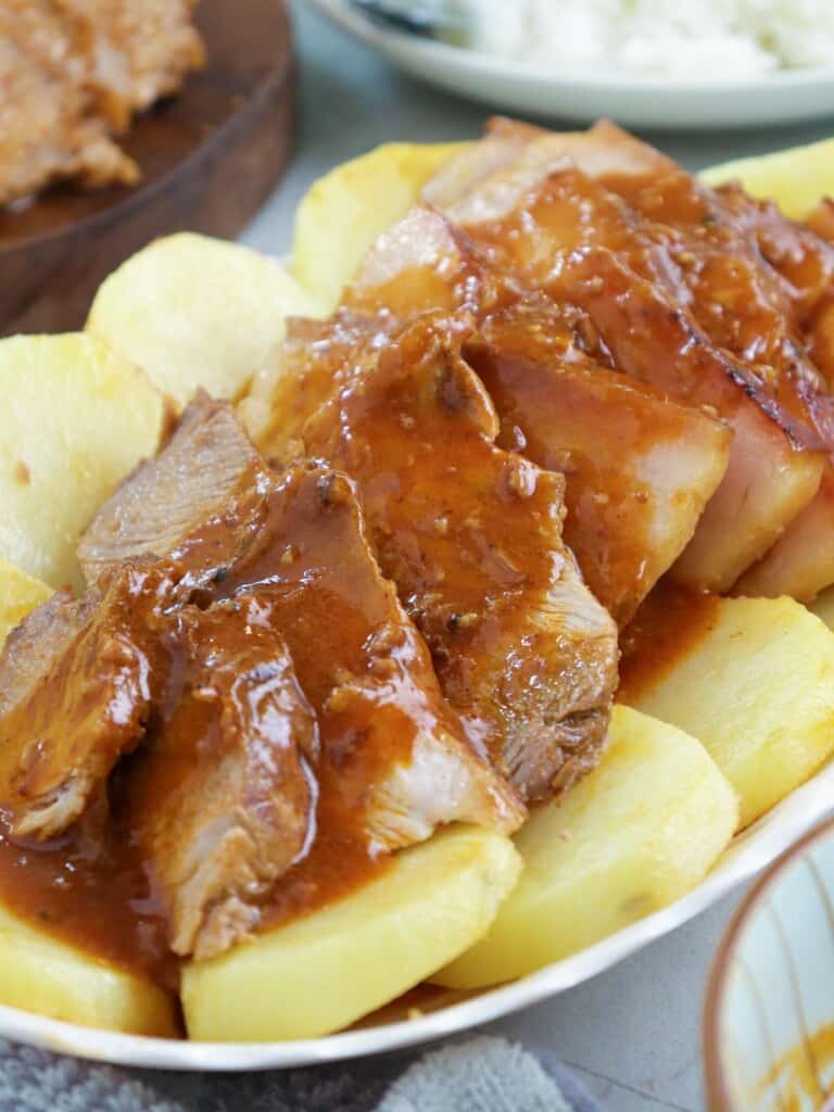 sliced Kapampangan-style asado with fried potato slices and tomato gravy on a serving platter