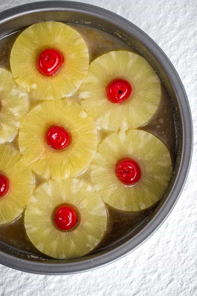 butter, brown sugar, pineapple rings, and maraschino cherries in a round pan