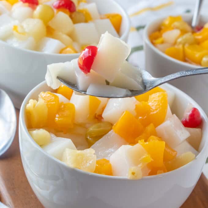 serving almond jelly with canned fruit with a spoon from a white serving bowl