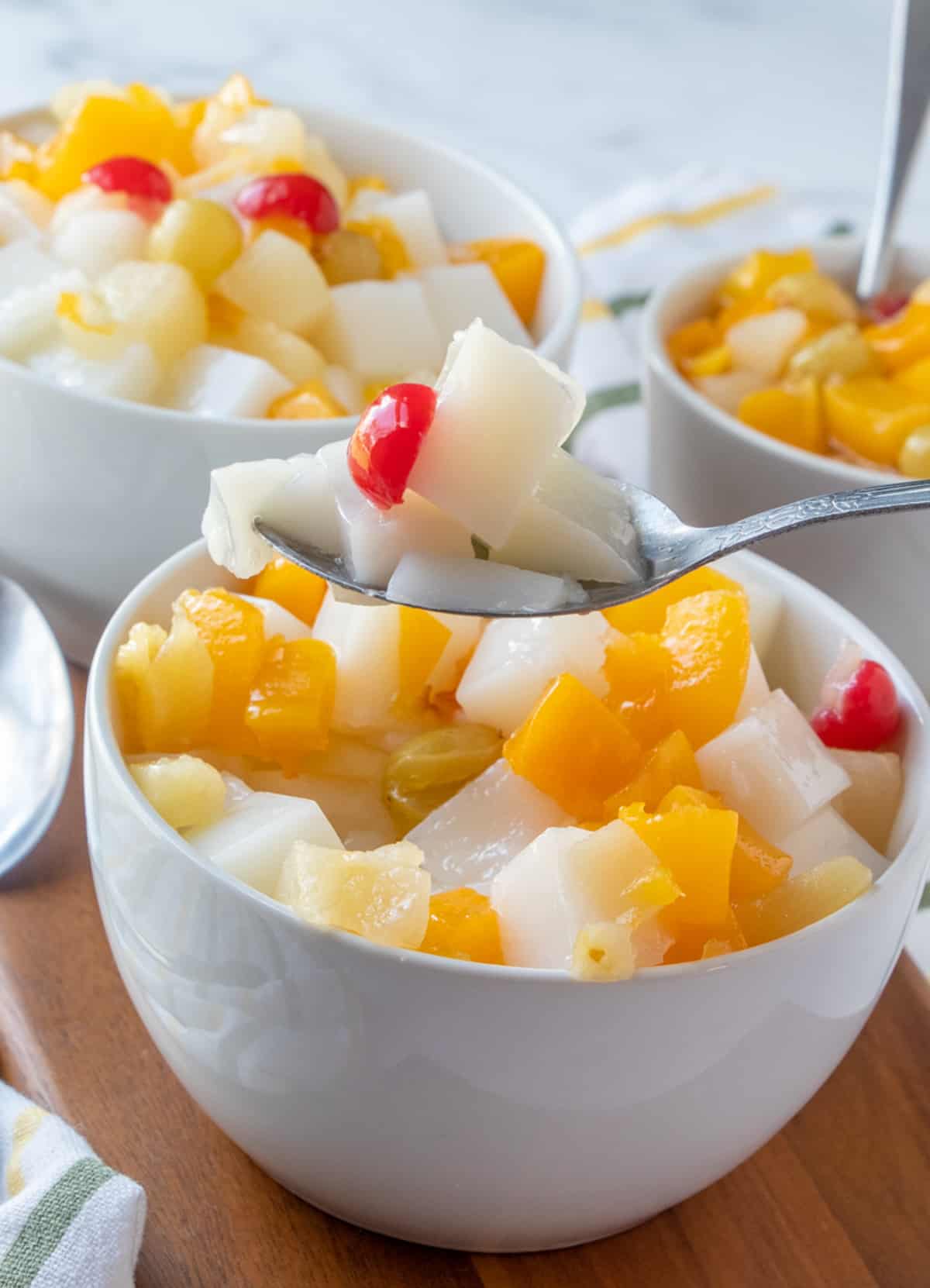serving almond jelly with canned fruit with a spoon from a white serving bowl