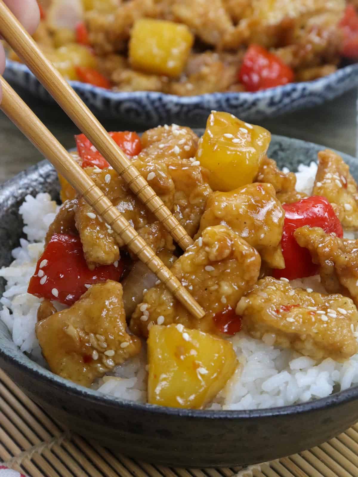 eating sweet fire chicken with chopsticks in a bowl over rice