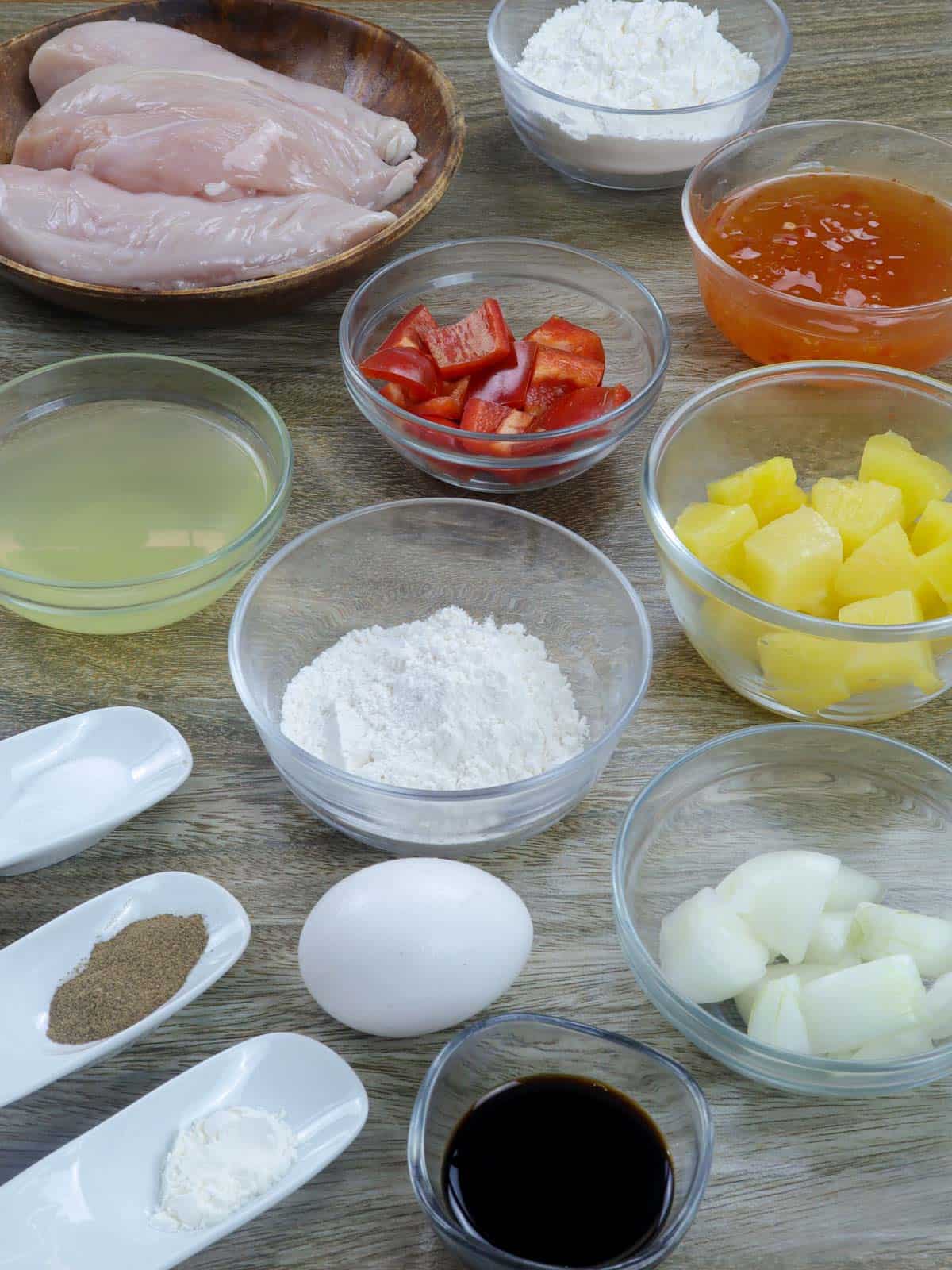 chicken, bell peppers, pineapple chunks, sweet chili sauce, garlic, salt, pepper, cornstarch, soy sauce, pineapple juice, oil, egg, flour in bowls