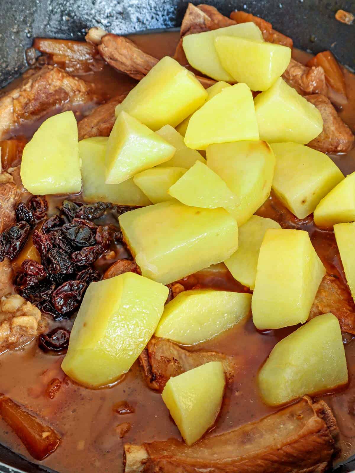 pork ribs cooked with pineapple juice, potatoes, and riasins in a pan