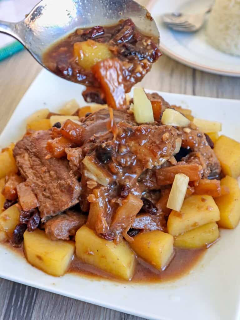 pouring sweet and savory pineapple sauce over pork ribs with pineapple on a white plate