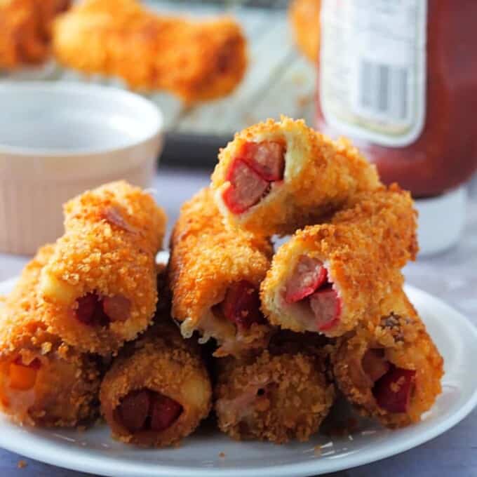 cheese and hot dog bread rolls on a white plate with ketchup on the side