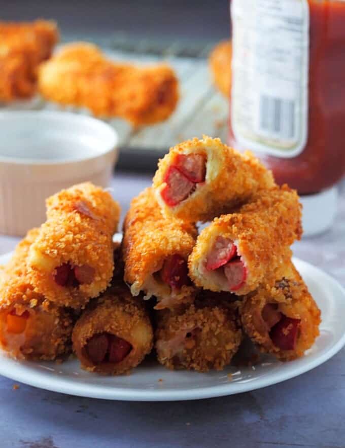 cheese and hot dog bread rolls on a white plate with ketchup on the side