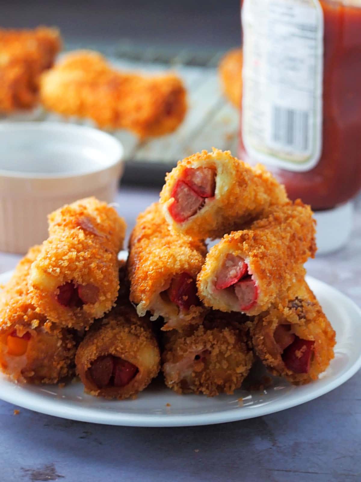 cheese and hot dog bread rolls on a white plate with ketchup on the side