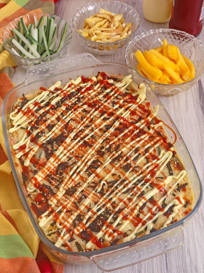 cheesy baked sushi in clear casserole dish with sliced mangoes, cucumbers, and egg omelet on the side