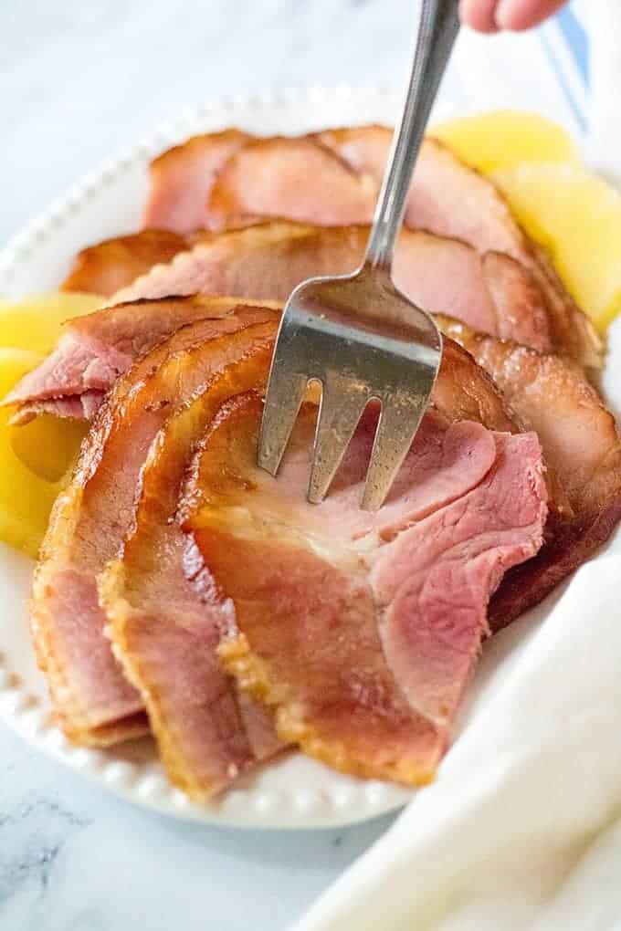 serving slices of slow cooker ham with a fork