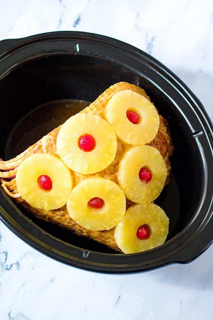 bone-in ham decorated with pineapple rings and maraschino cherries in a crockpot