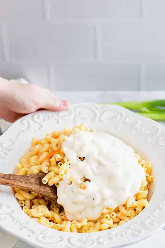 mixing macaroni with mayonnaise dressing in a white bowl