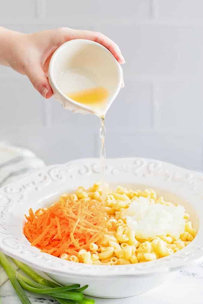 pouring apple cider to a bowl of macaroni, shredded carrots, and mayo dressing