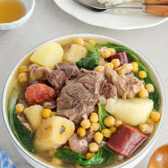 filipino-style beef soup in a bowl with a plate of steamed rice in the backbround.