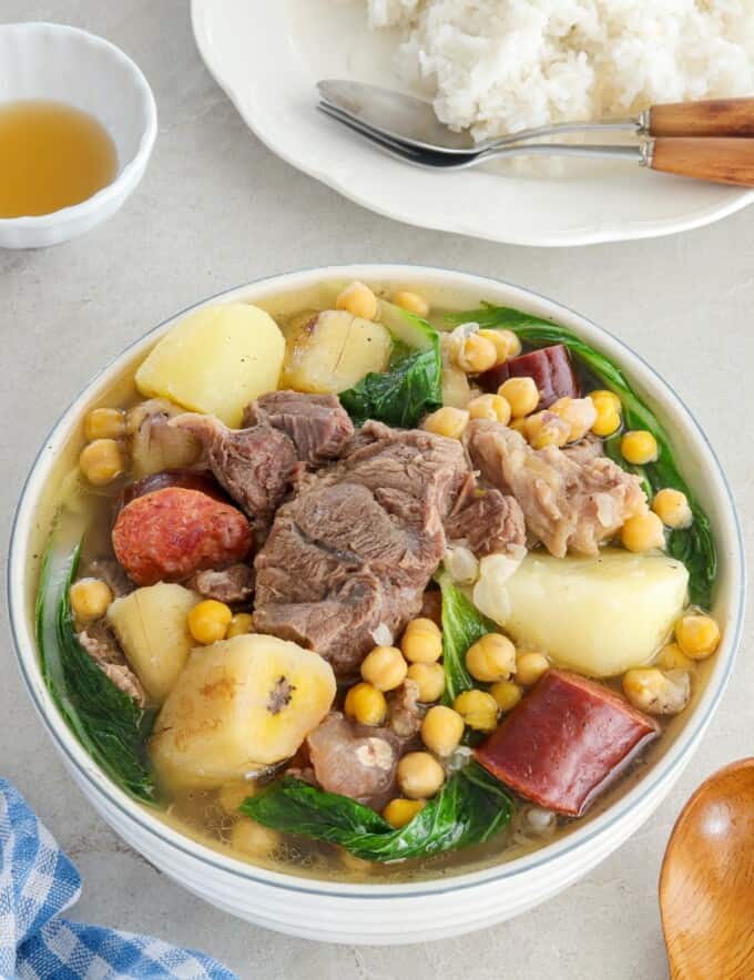 filipino-style beef soup in a bowl with a plate of steamed rice in the backbround.