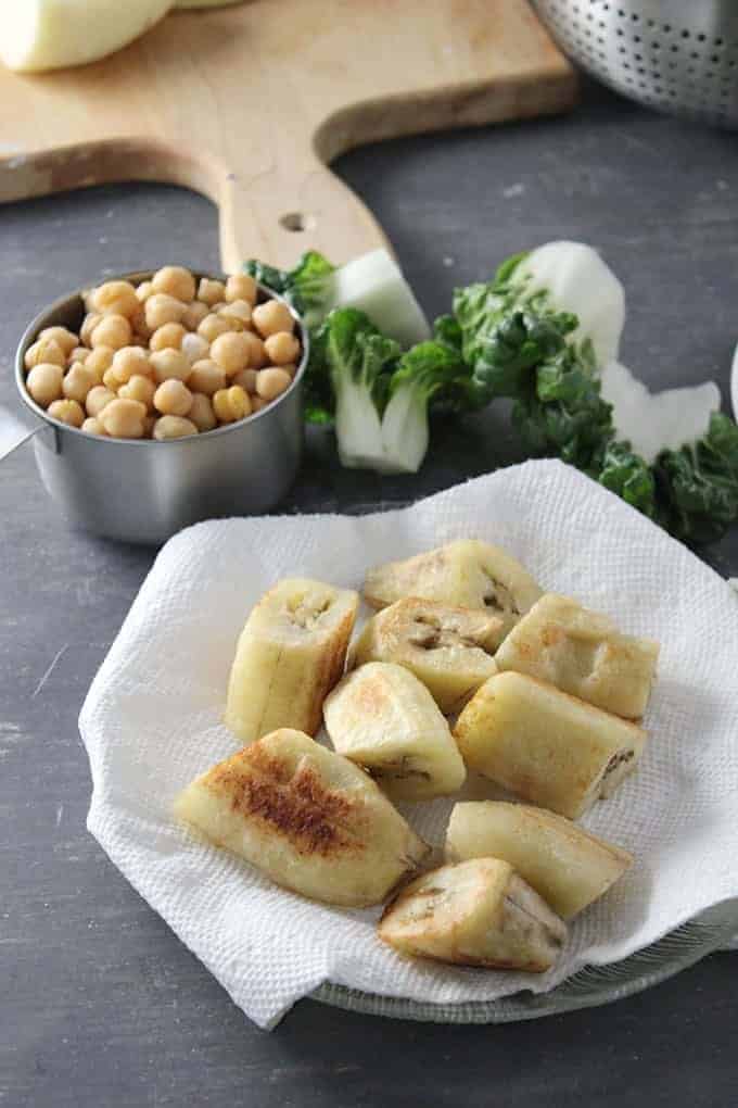 pan-fried saba bananas on a white plate with garbanzo beans and pechay on the side