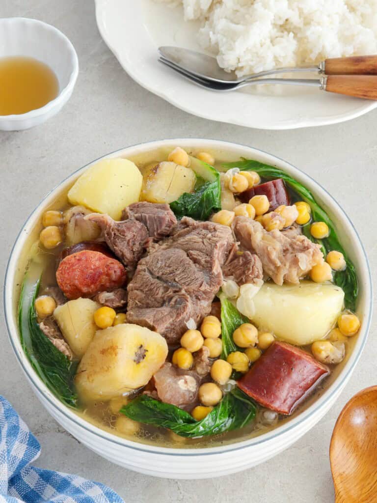 filipino-style beef soup in a bowl with a plate of steamed rice in the backbround.