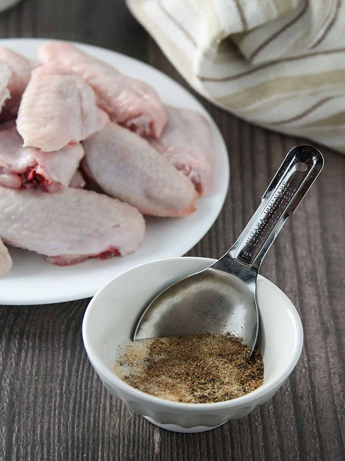 tamarind powder, salt, garlic powder, pepper in a bowl with chicken wings in another bowl on the side