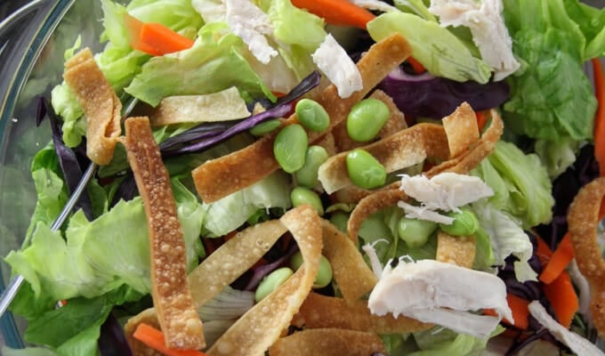 Chinese Chicken Salad in a large glass bowl with a plate of salad and a jar of dressing on the side