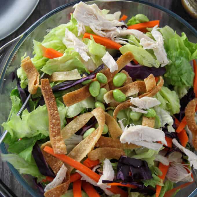 Chinese Chicken Salad in a large glass bowl with a plate of salad and a jar of dressing on the side