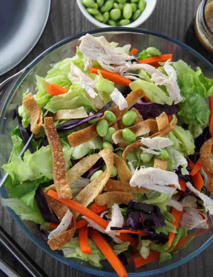 Chinese Chicken Salad in a large glass bowl with a plate of salad and a jar of dressing on the side