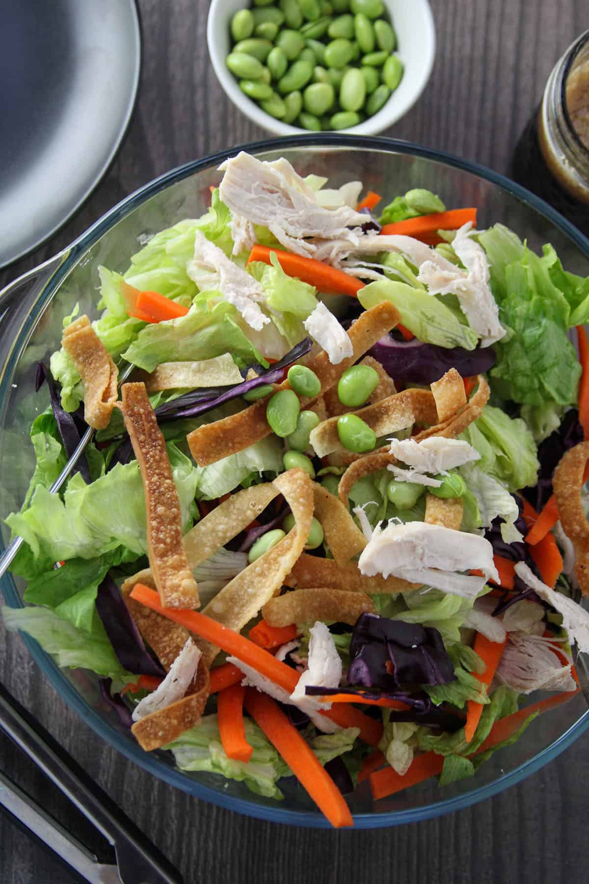 Chinese Chicken Salad in a large glass bowl with a plate of salad and a jar of dressing on the side