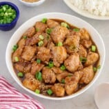 Sesame Chicken in a bowl with a plate of steamed rice in the background.