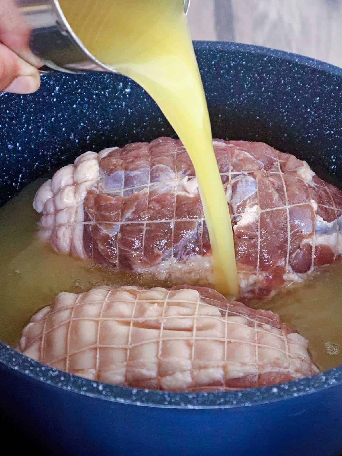 pouring pineapple juice over cured pork ham in a pot
