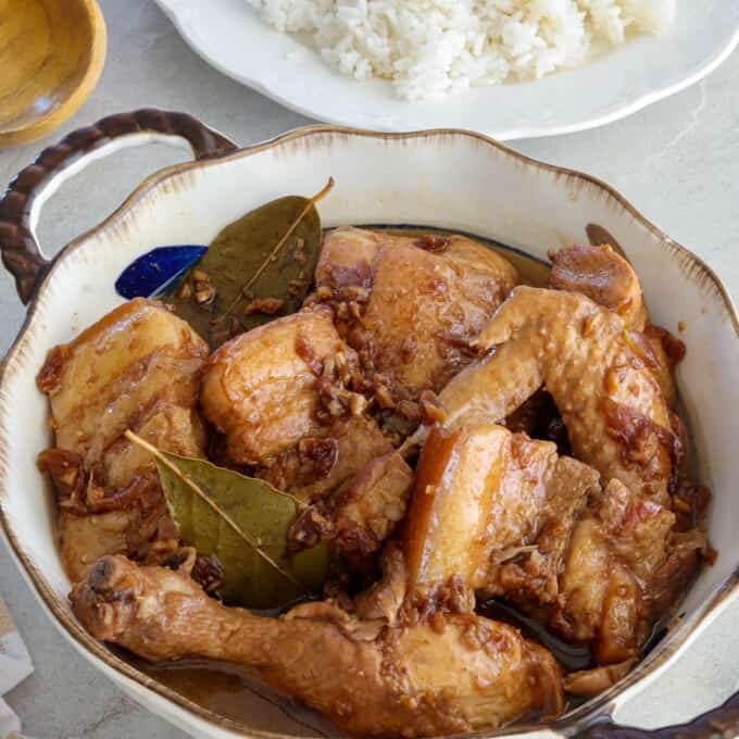 Chicken and Pork Adobo in a serving bowl with a plate of steamed rice in the background.