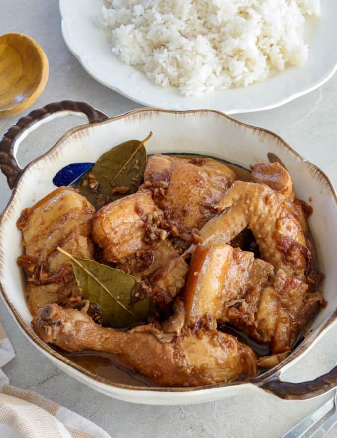 Chicken and Pork Adobo in a serving bowl with a plate of steamed rice in the background.