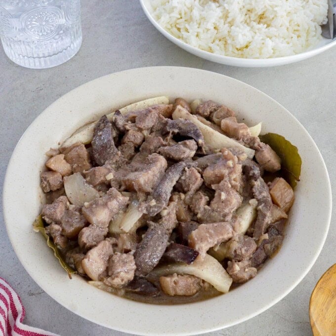 Kilawing Labanos at Baboy in a white serving bowl with a plate of rice in the background.