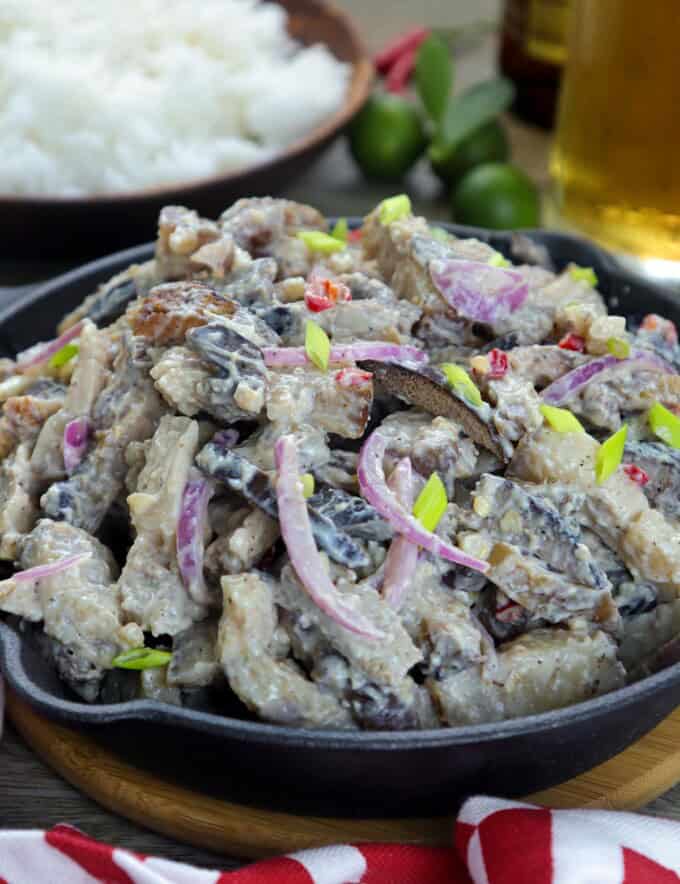 Dinakdakan in a cast iron skillet with a bowl of steamed rice on the side and a glass of beer.