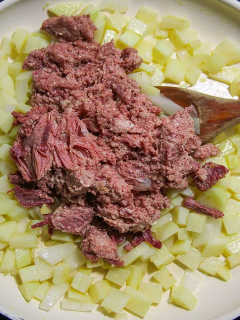 corned beef with diced potatoes, garlic, and onions in a pan