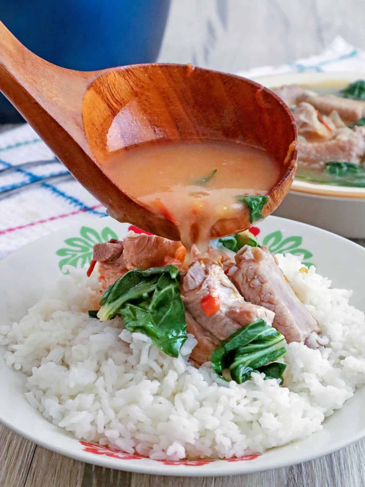 pouring broth over pork kinamatisan on steamed rice on a white plate