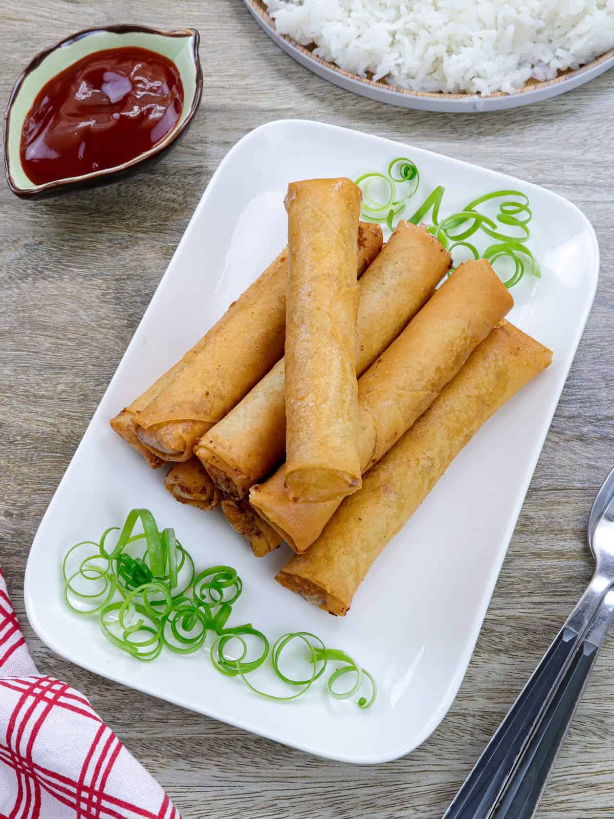 tuna spring rolls on a serving platter with a small bowl of ketchup sauce on the side.