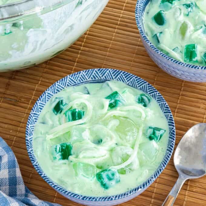 Buko Pandan Salad in a clear glass bowl and in small blue bowls with spoon in the background.