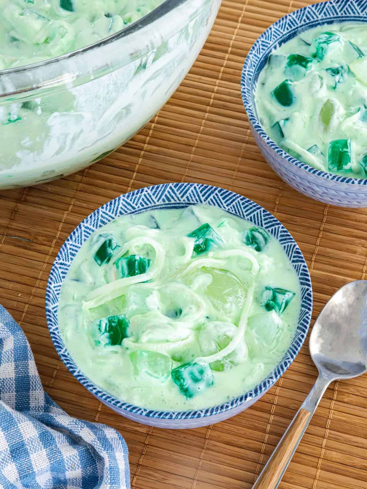 Buko Pandan Salad in a clear glass bowl and in small blue bowls with spoon in the background.