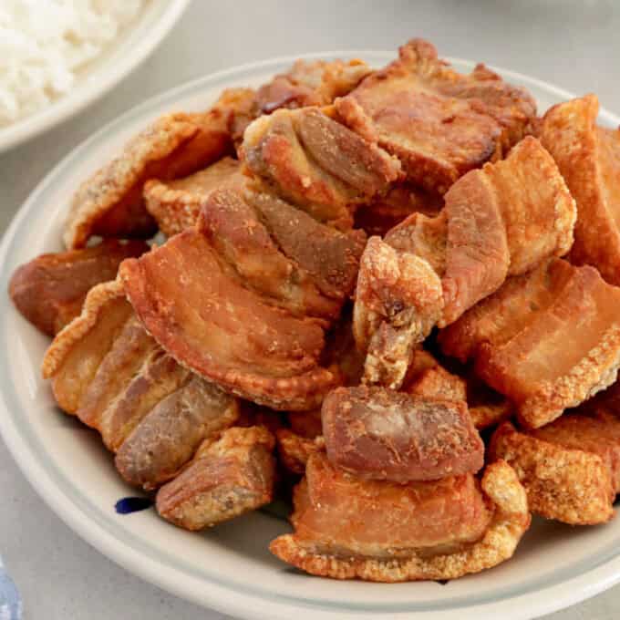 crispy pork belly in a white serving bowl with steamed rice and vinegar dipping sauce in the background.