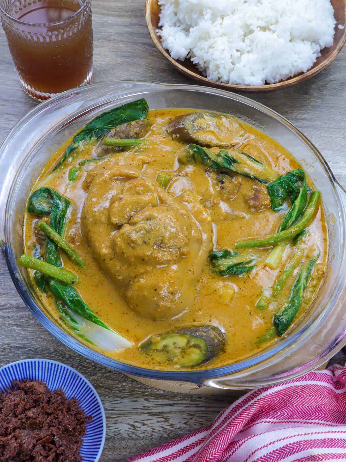 Pork kare kare in a clear glass bowl with steamed rice and ginisang bagoong on the side