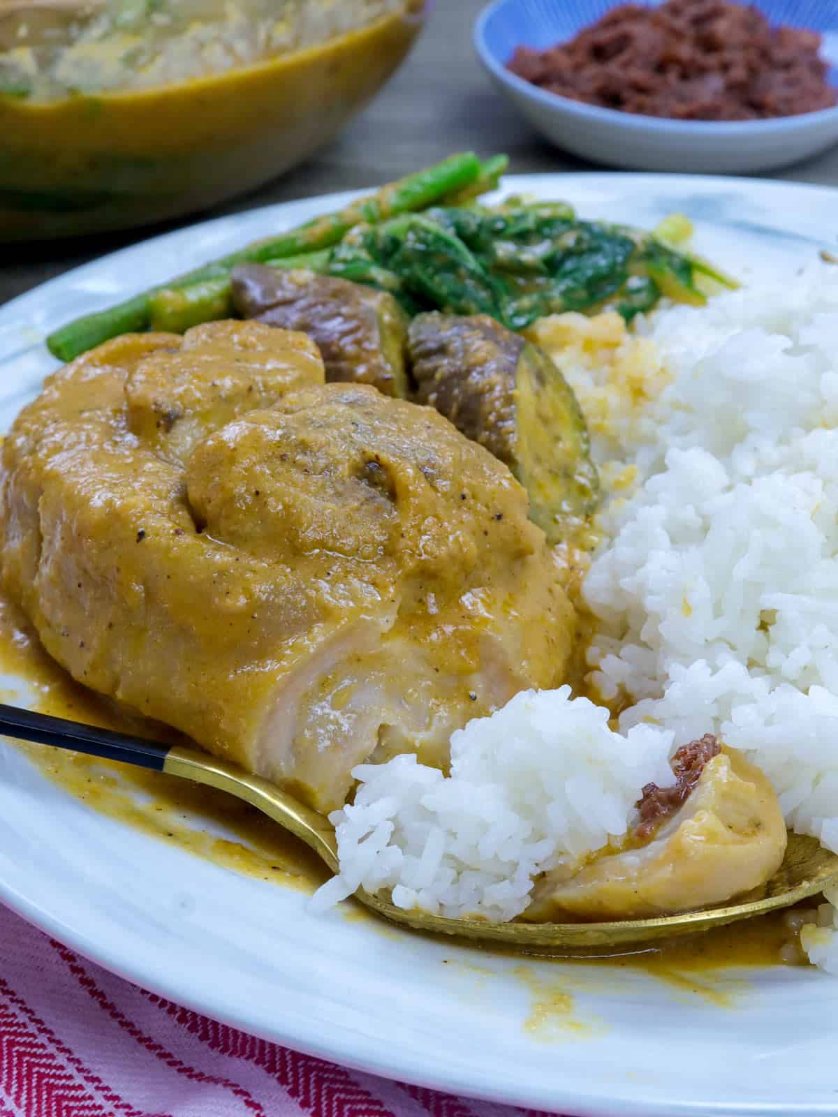 eating pork kare kare on a white plate with steamed rice