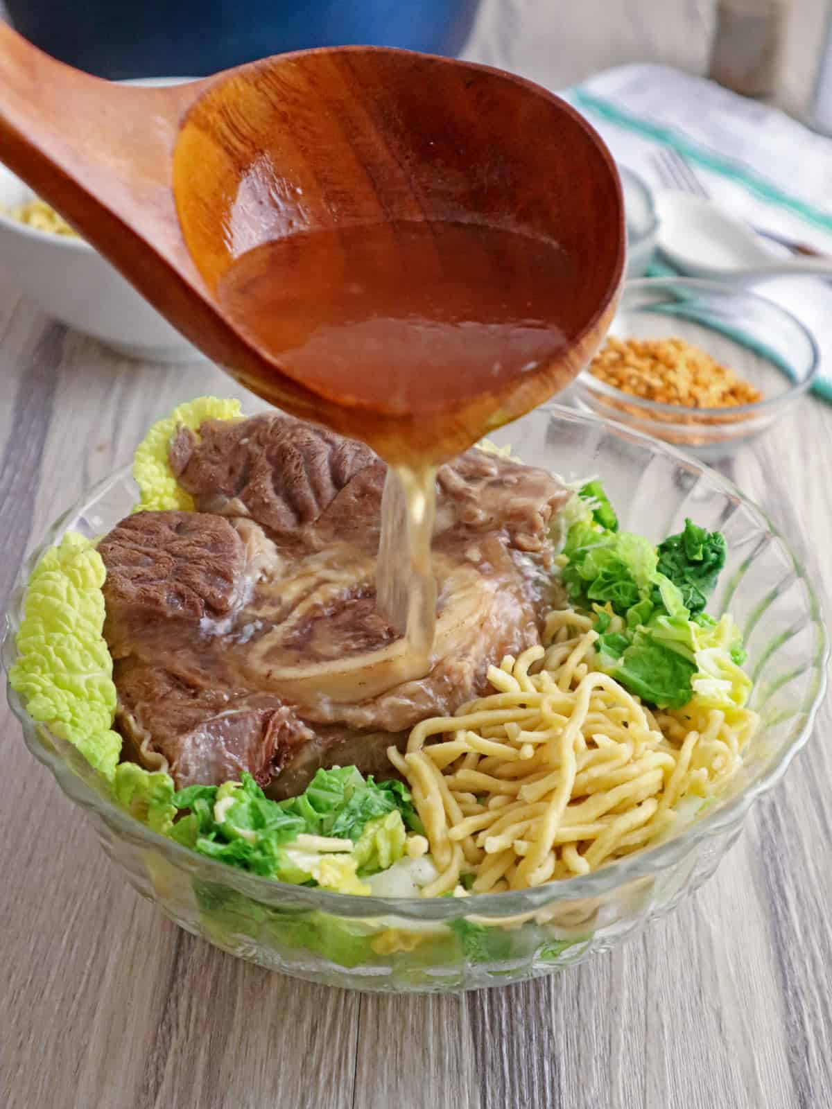 pouring hot broth to a bowl of beef, noodles, and cabbage